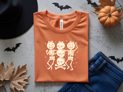 Orange t-shirt with a graphic of dancing skeletons and skulls with bows and sparkles.