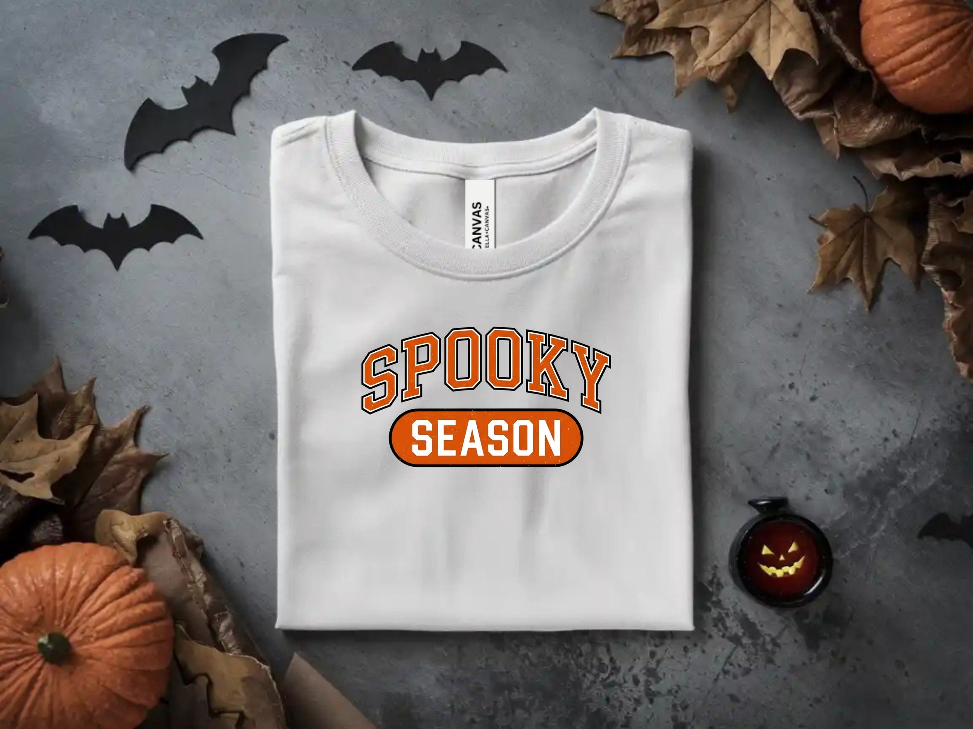 White t-shirt with orange text "SPOOKY SEASON" on a Halloween-themed background.