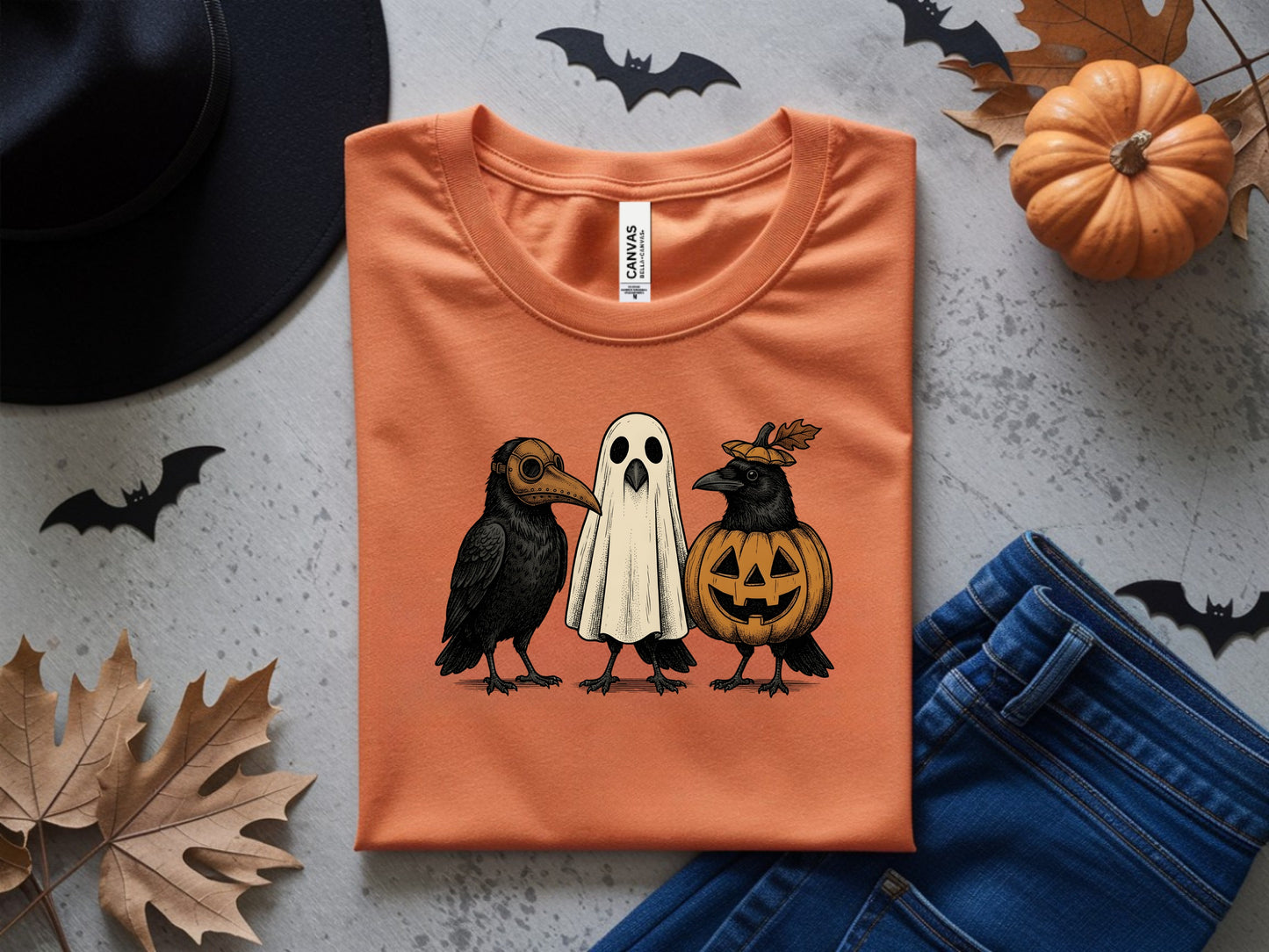 Orange t-shirt with Halloween crows dressed as a plague doctor, ghost, and pumpkin.