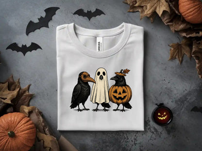 White t-shirt featuring three cartoon birds dressed as Halloween characters: one in a plague doctor mask, one as a ghost, and one as a pumpkin.