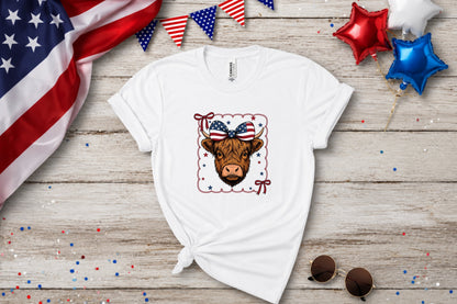 White t-shirt with a Highland cow wearing a patriotic bow and stars.
