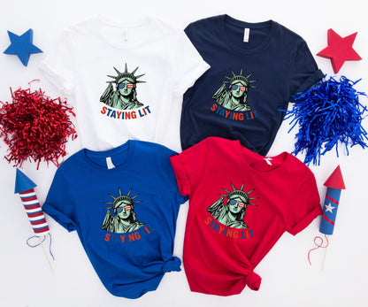Four t-shirts featuring the Statue of Liberty and "STAYING LIT" text.