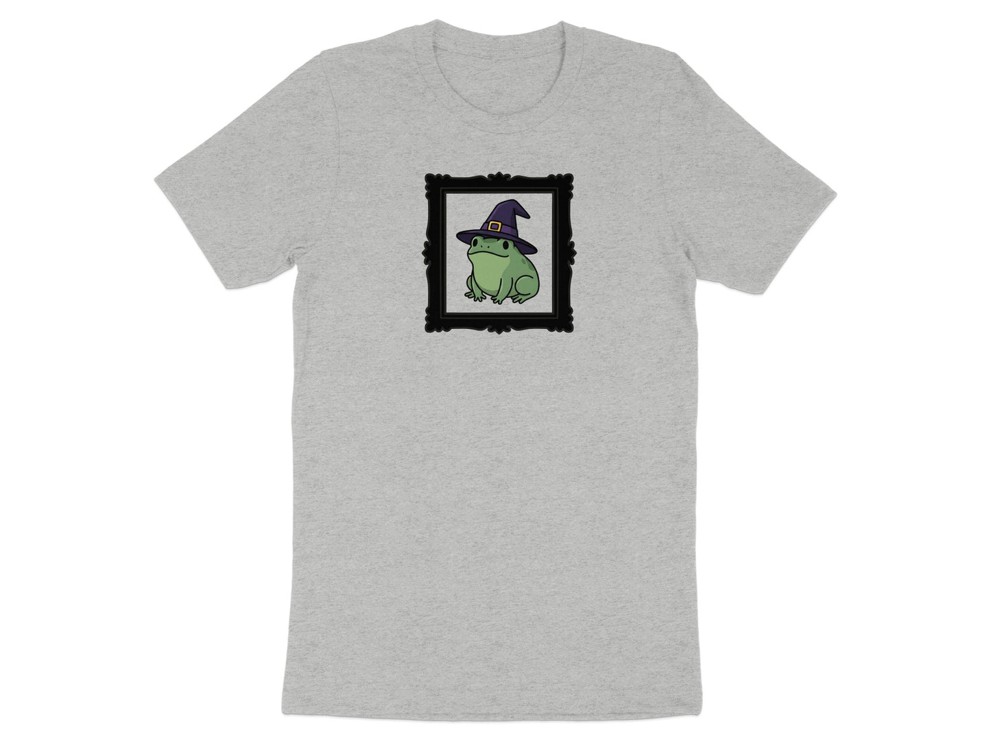 Green frog wearing witch hat in black ornate frame on grey t-shirt.