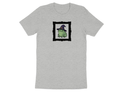 Green frog wearing witch hat in black ornate frame on grey t-shirt.