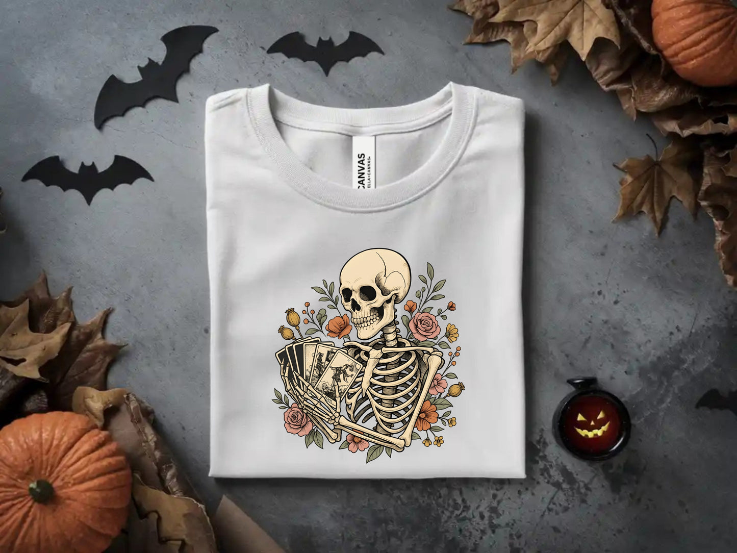 Skeleton holding tarot cards surrounded by flowers on a white t-shirt.