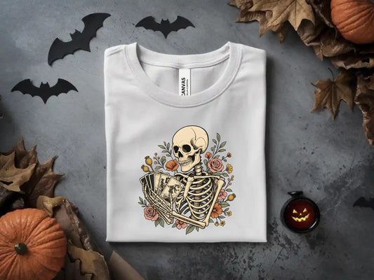 Skeleton holding tarot cards surrounded by flowers on a white t-shirt.