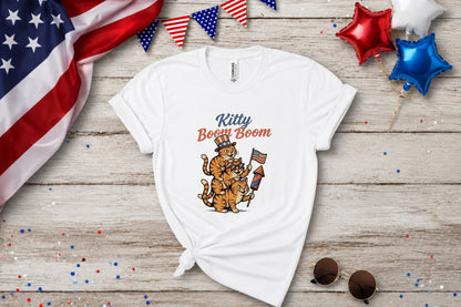 White t-shirt with cartoon cats holding fireworks and wearing patriotic hats.
