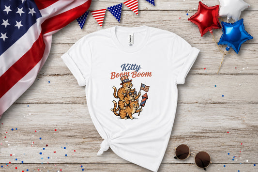 White t-shirt with cartoon cats holding fireworks and wearing patriotic hats.