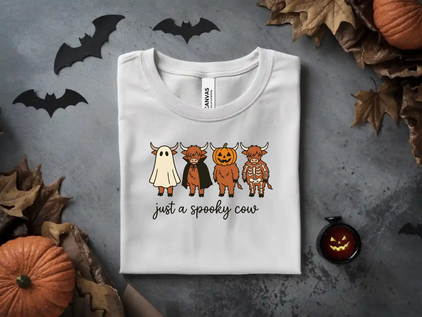 White t-shirt with graphic of four cows in Halloween costumes and text "just a spooky cow."