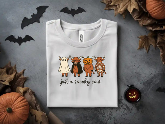 White t-shirt with graphic of four cows in Halloween costumes and text "just a spooky cow."