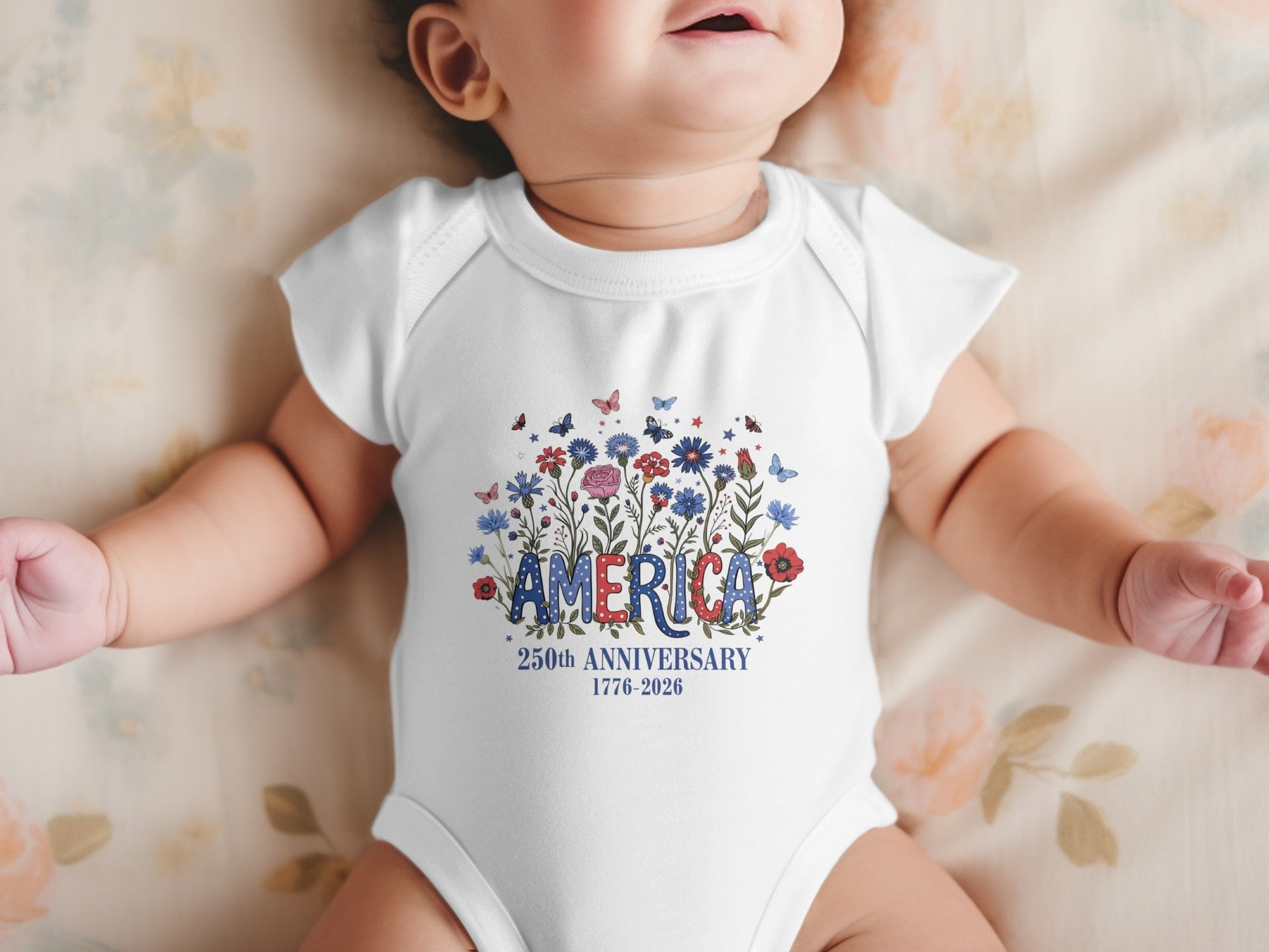 Baby in a white bodysuit with "America 250th Anniversary 1776-2026" and floral design.