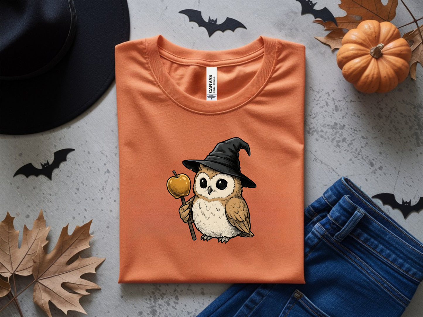 Orange t-shirt with a graphic of a kawaii owl wearing a witch hat holding a candy apple.