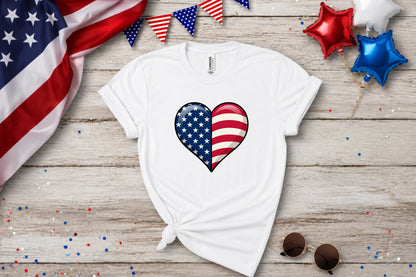 White t-shirt with a split USA flag heart design, adorned with confetti and balloons.