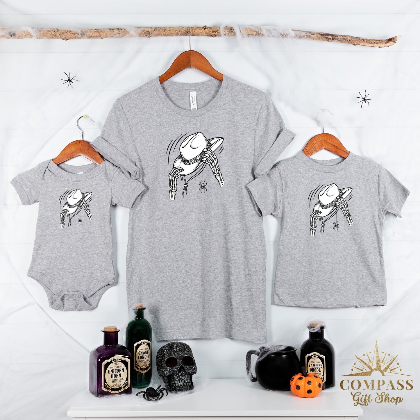 Three grey t-shirts, featuring a skeleton's hands holding a cowboy hat with a spider hanging.