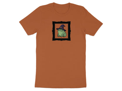 Green frog wearing a purple witch hat inside a black picture frame on an orange t-shirt.