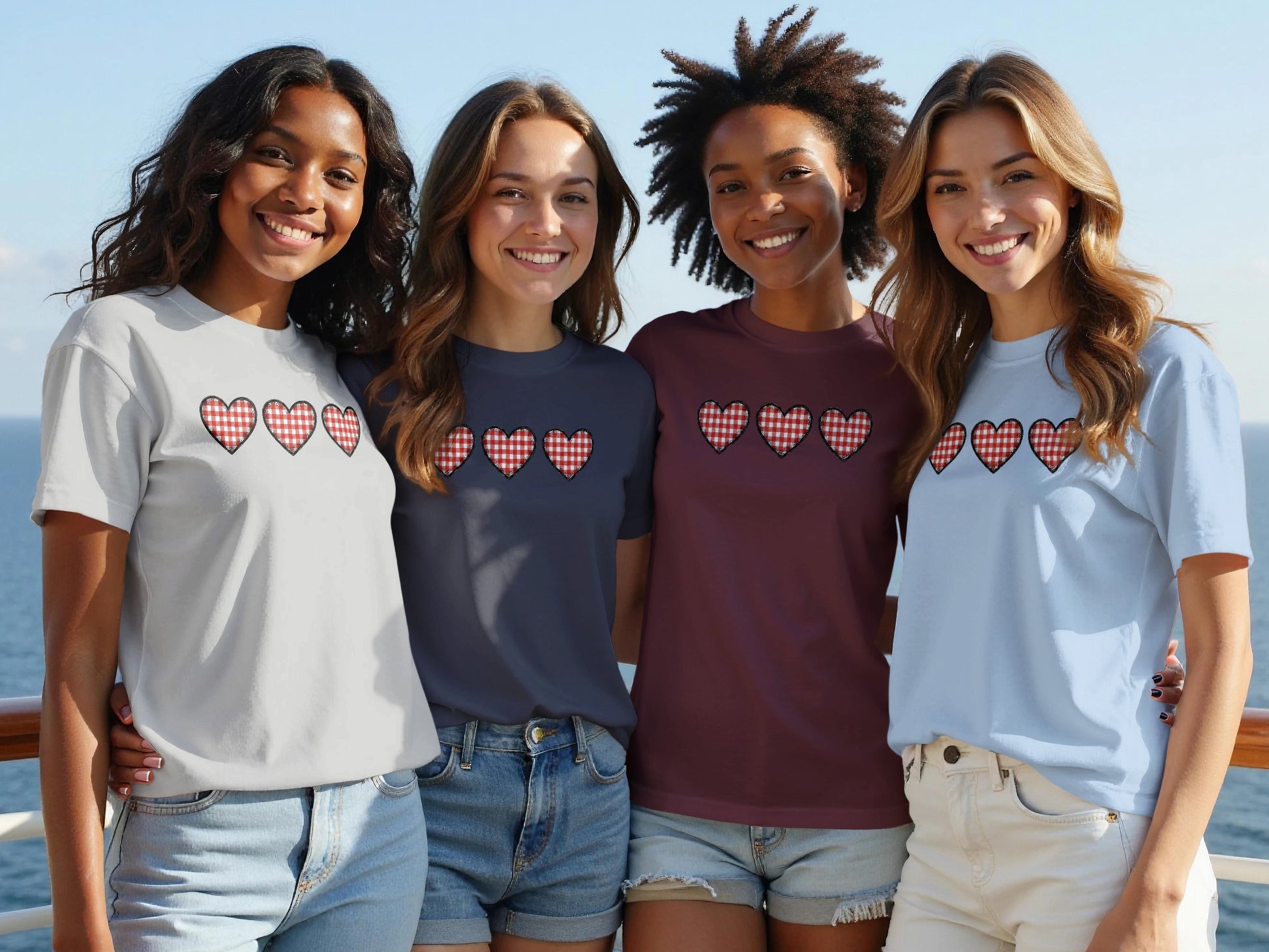 Four smiling women wear t-shirts with a repeating red and white checkered heart pattern.