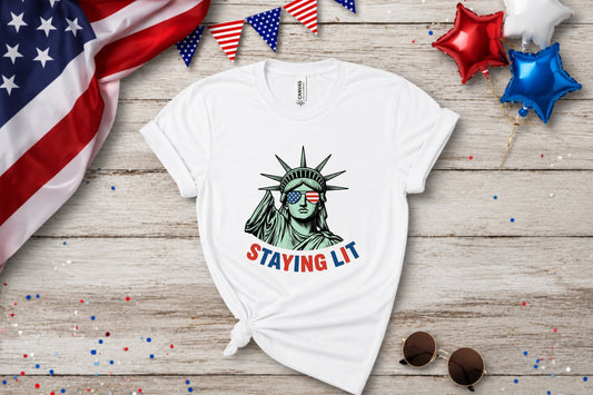 White t-shirt with Statue of Liberty wearing sunglasses and "STAYING LIT" text.
