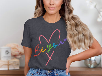Dark t-shirt with "be your own" heart design in rainbow colors.