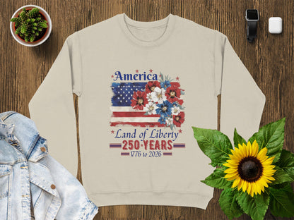 Light tan sweatshirt with "America Land of Liberty 1776-2026" text and US flag floral design.