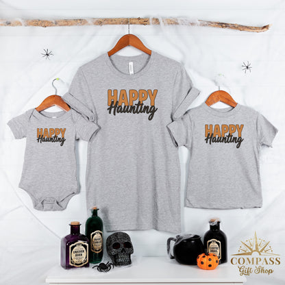 Grey t-shirts and baby onesie with "HAPPY Haunting" text; Halloween props displayed.