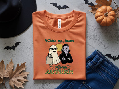 Orange t-shirt with ghost and vampire graphic saying "Wake up, loser it's officially Autumn"