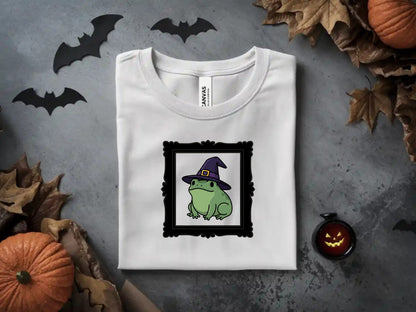 White t-shirt with a framed cartoon frog wearing a witch hat.