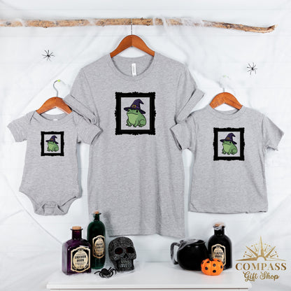 Grey t-shirts and a bodysuit feature a frog in a witch hat graphic.