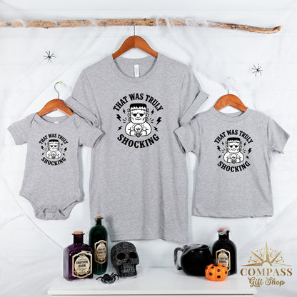 Grey t-shirts and baby onesie with Frankenstein and lightbulb graphic stating "That was truly shocking".