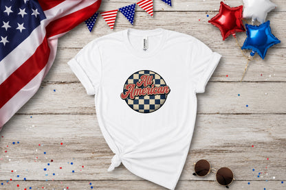 White t-shirt with "All American" in a checkered circle, on wooden background.