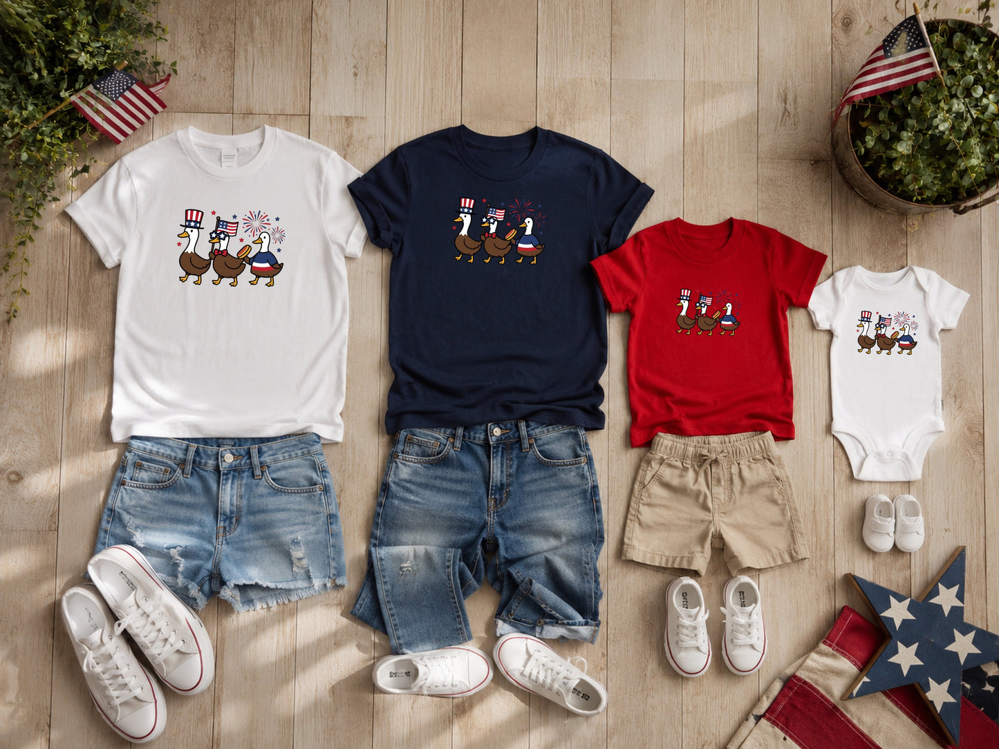 Four patriotic t-shirts and onesie with ducks on wooden background.