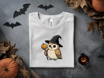 White t-shirt with an owl in a witch hat holding a candy apple.