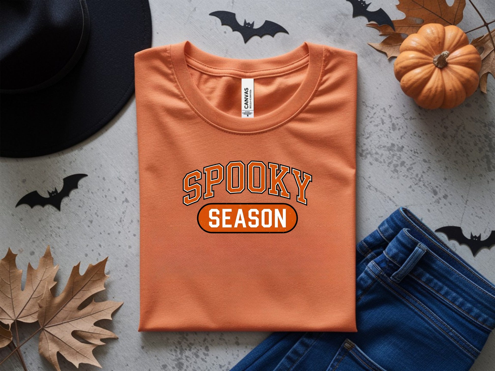 Orange t-shirt with "SPOOKY SEASON" text, Halloween decorations, and jeans.
