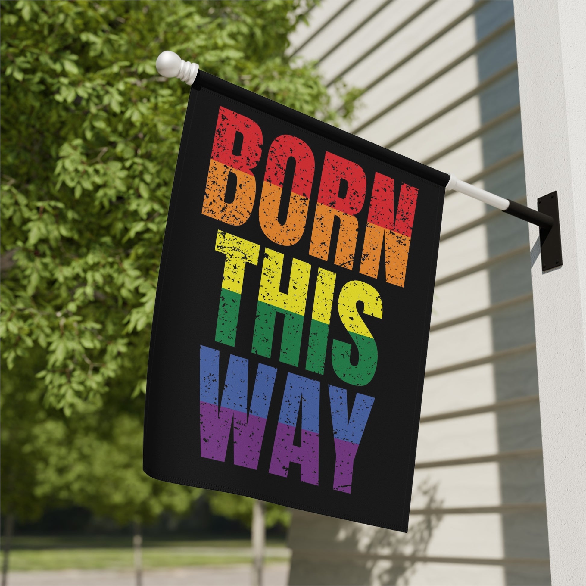 Black flag with "BORN THIS WAY" in rainbow colors, mounted on a pole.