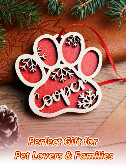 Decorative paw print ornament with 'Cooper' on a wooden surface with Christmas decorations.