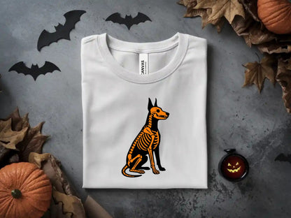 White t-shirt with a Doberman skeleton graphic, surrounded by Halloween decorations.