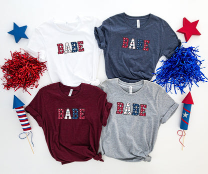 Four t-shirts with "BABE" in a star-spangled banner pattern.