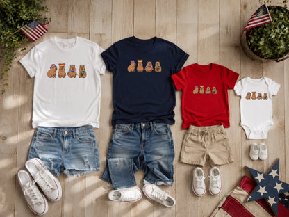 Capybaras wearing festive hats on white, navy, and red t-shirts and onesie.