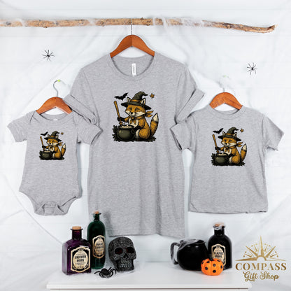 Grey t-shirts and onesie display a Halloween fox graphic with a witch hat and cauldron.