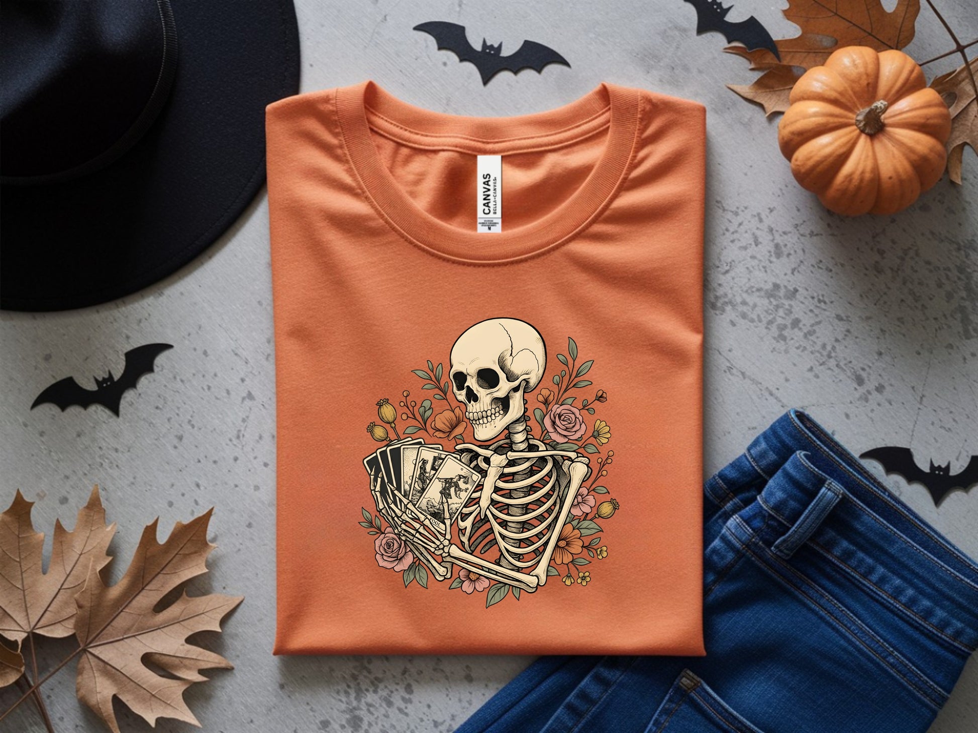 Orange t-shirt with skeleton holding tarot cards and floral design.