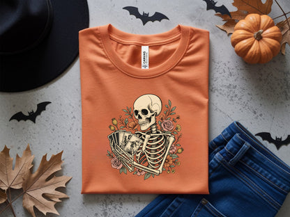 Orange t-shirt with skeleton holding tarot cards and floral design.
