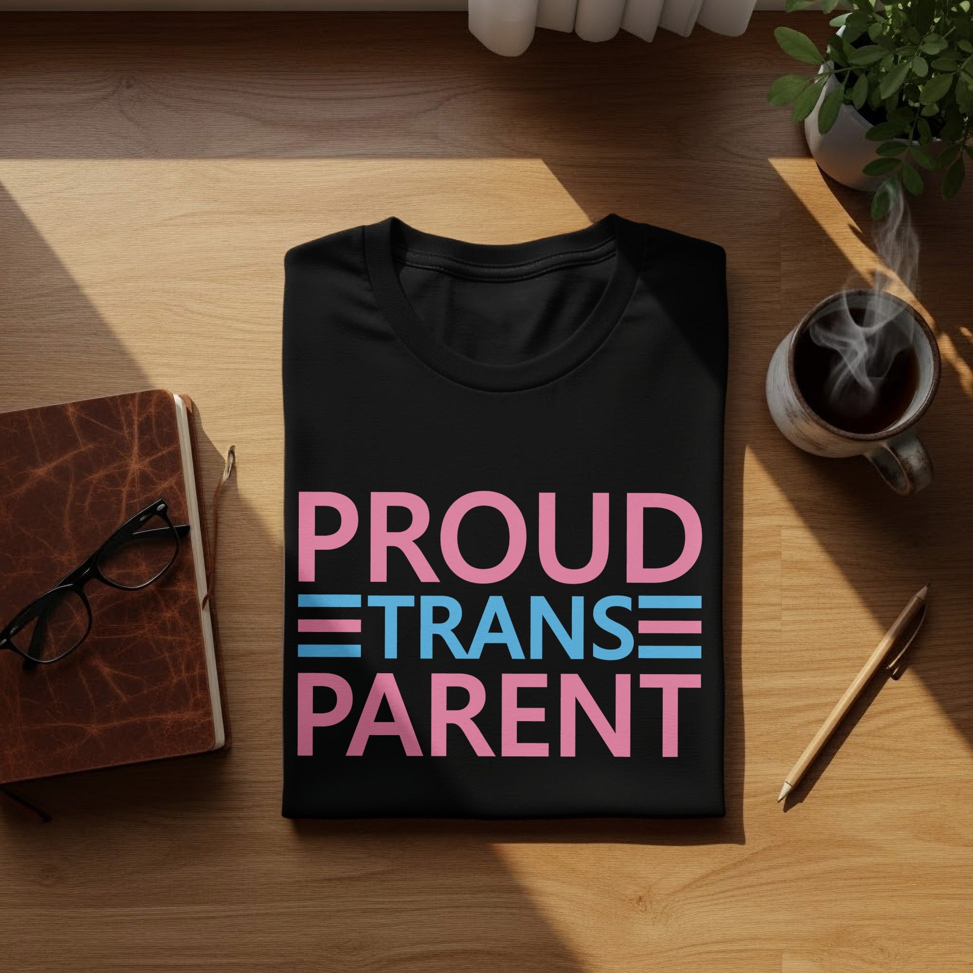Black t-shirt with "PROUD TRANS PARENT" text in pink and blue stripes.