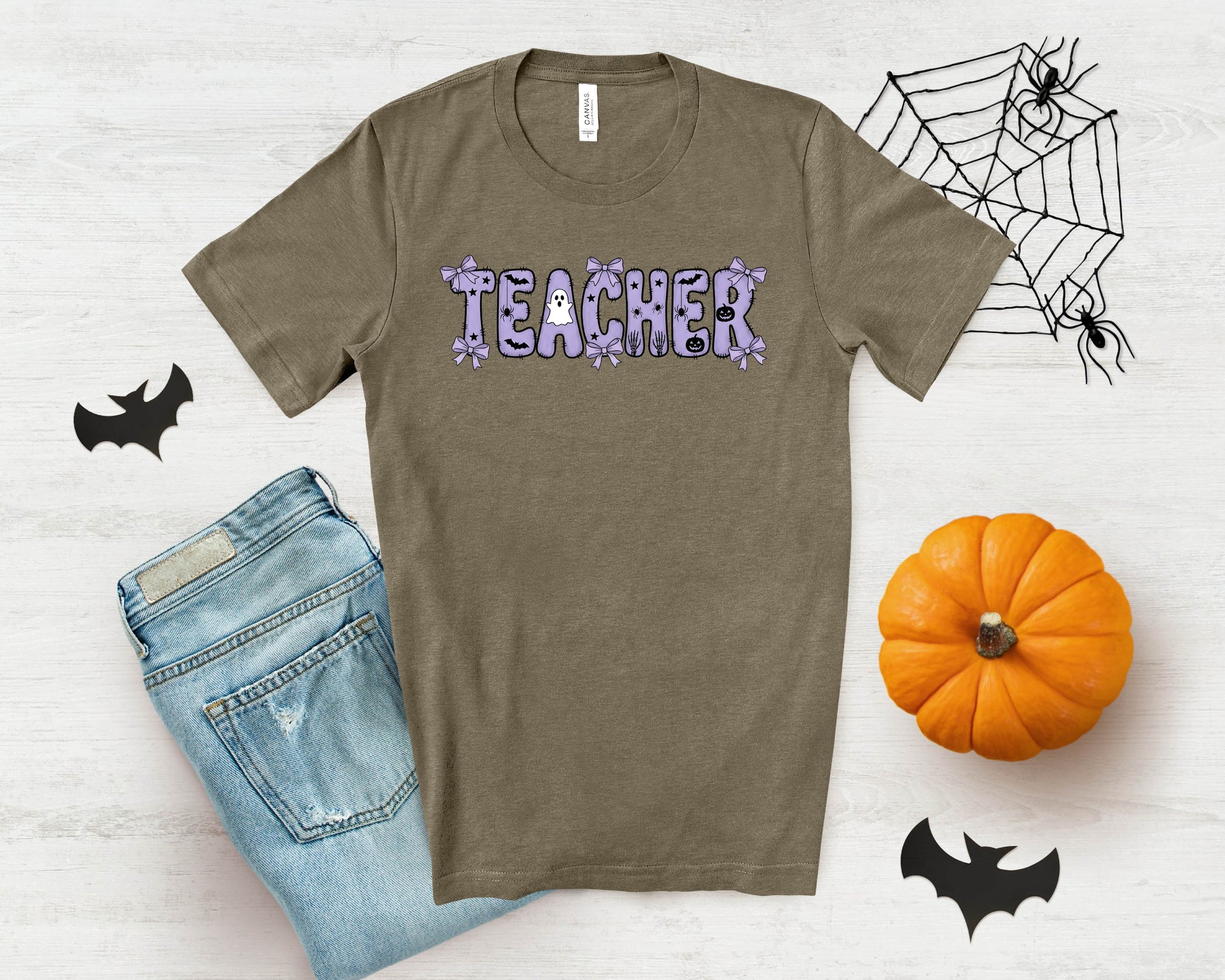 Brown t-shirt with "TEACHER" in purple Halloween font, next to jeans and a pumpkin.