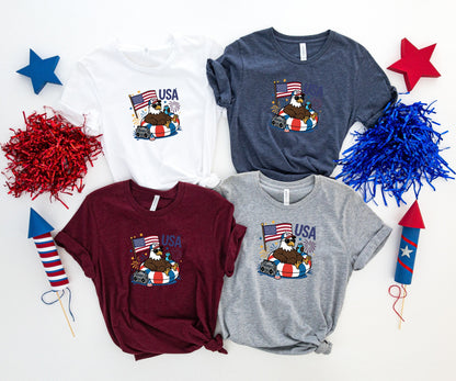 Four t-shirts featuring an eagle with sunglasses and headphones holding an American flag.