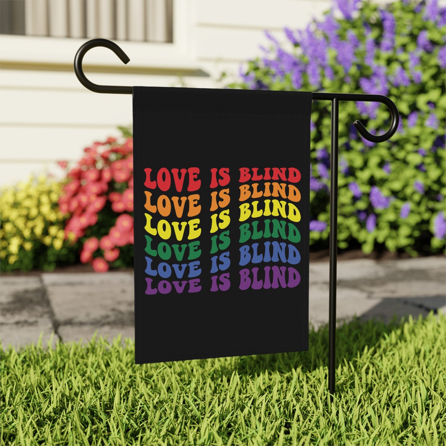 Black garden flag with rainbow text reading "LOVE IS BLIND" repeated six times.