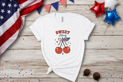 White t-shirt with "Sweet Liberty" text and cherry graphic on a wooden background.