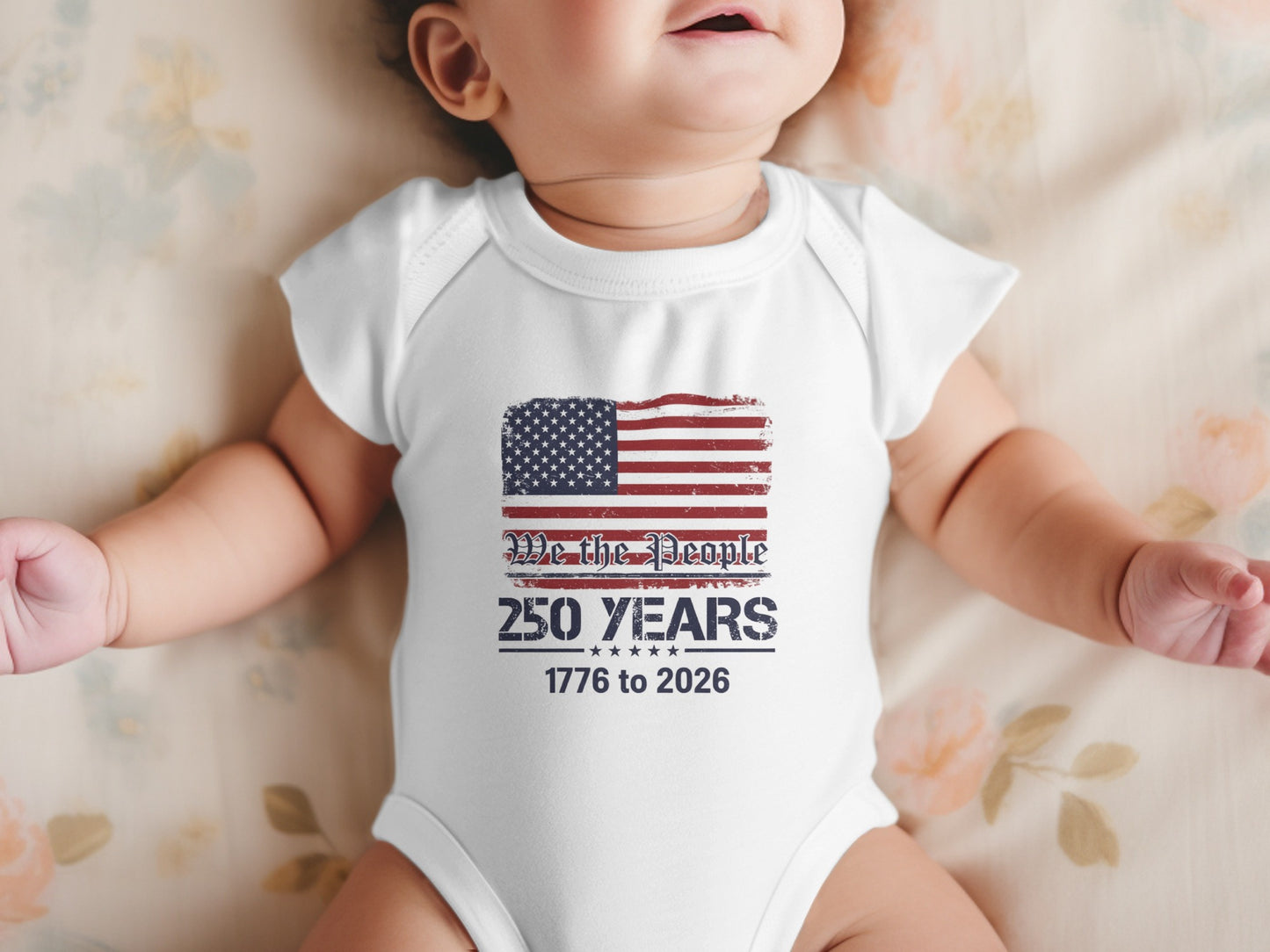 Baby in white onesie with American flag and "We the People" text.