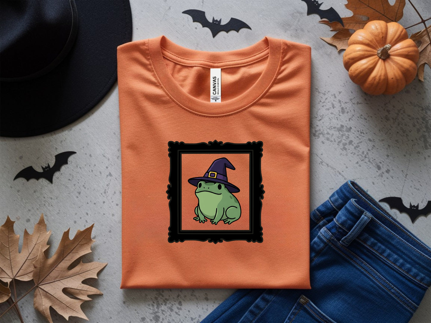 Orange t-shirt with black frame graphic of a frog wearing a witch hat.