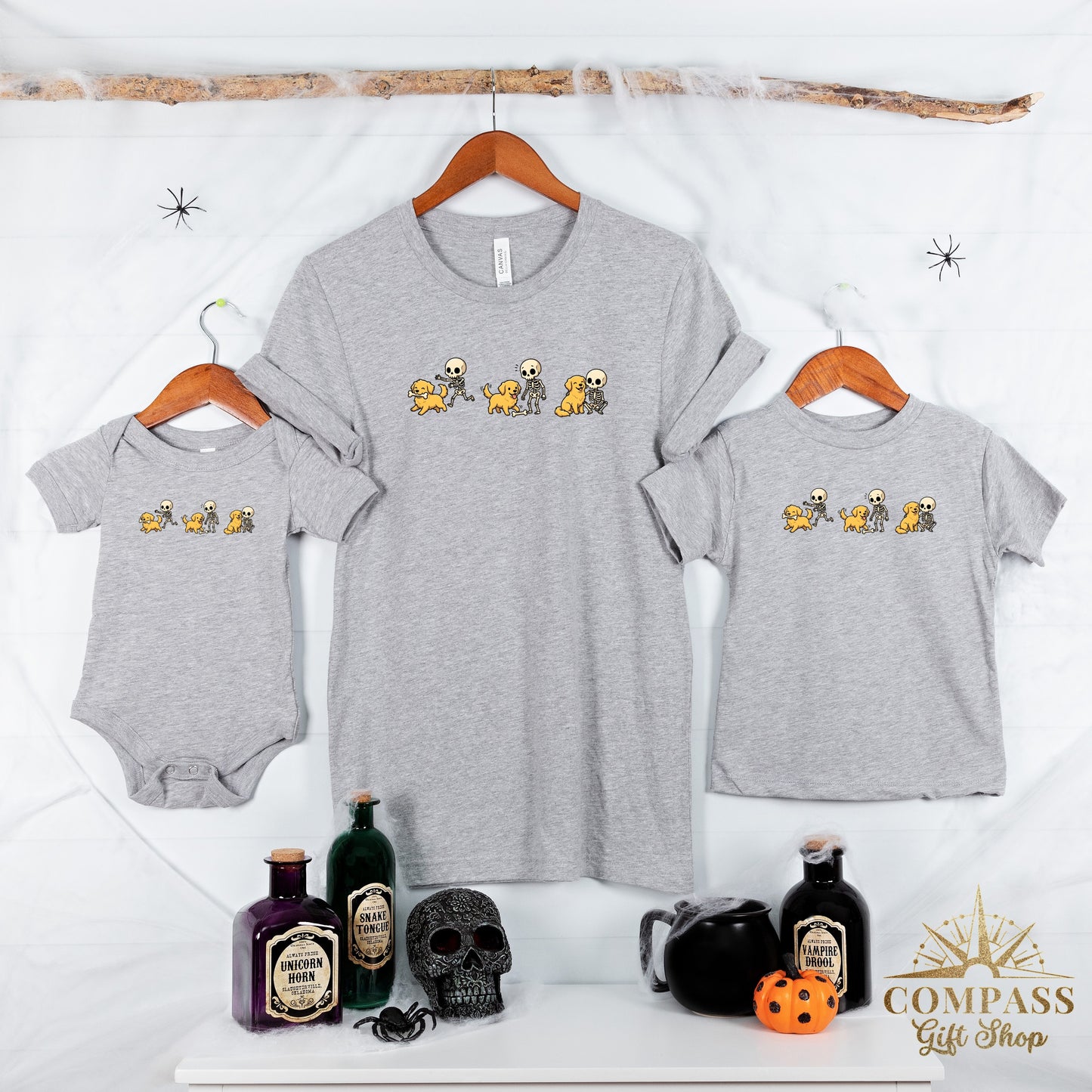 Grey shirts and a baby onesie feature a cartoon print of skeletons playing with dogs.