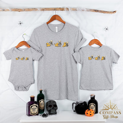 Grey shirts and a baby onesie feature a cartoon print of skeletons playing with dogs.