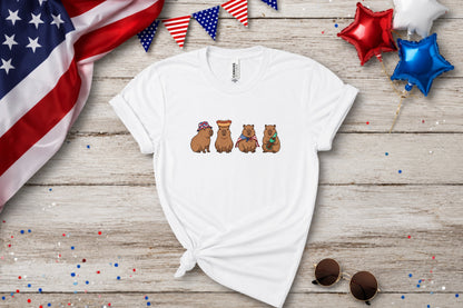White t-shirt with four capybaras wearing patriotic hats and accessories.